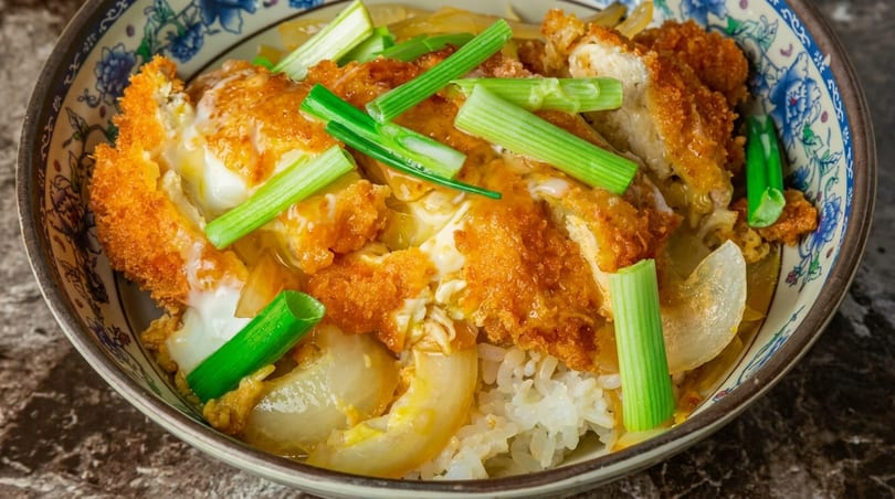 Close-up of Katsudon with crispy fried pork cutlets, egg, onions, and green onions over rice.