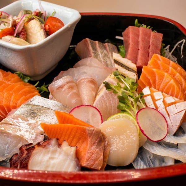A black and red tray filled with various sashimi, including salmon, tuna, and scallops, with a side salad.