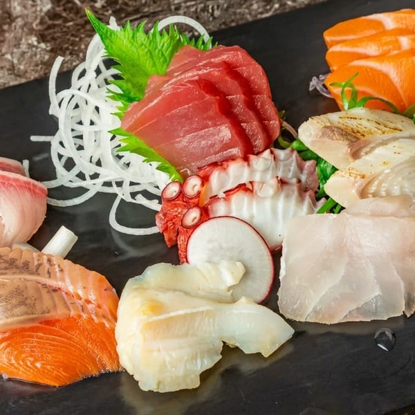 Assorted sashimi platter with tuna, salmon, octopus, and sea grapes on a dark slate.