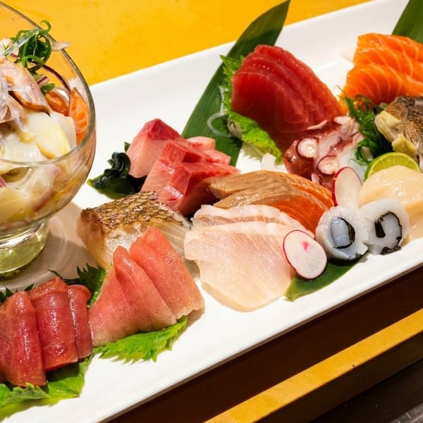 A large platter of various sashimi, including tuna, salmon, and scallops, with a side salad.