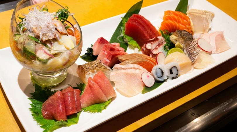 A large platter of various sashimi, including tuna, salmon, and scallops, with a side salad.