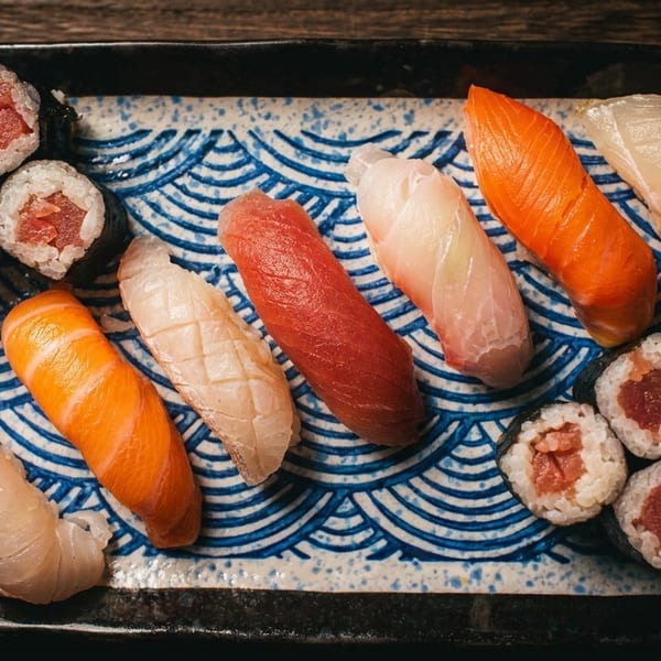 A rectangular plate of various sushi and sashimi pieces on a wooden table.