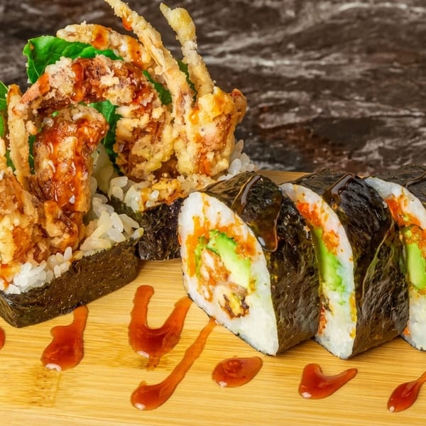 Soft shell crab sushi rolls with avocado and sauce on a wooden board.